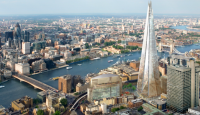 a tall glass tower next to a river with The Shard in the background