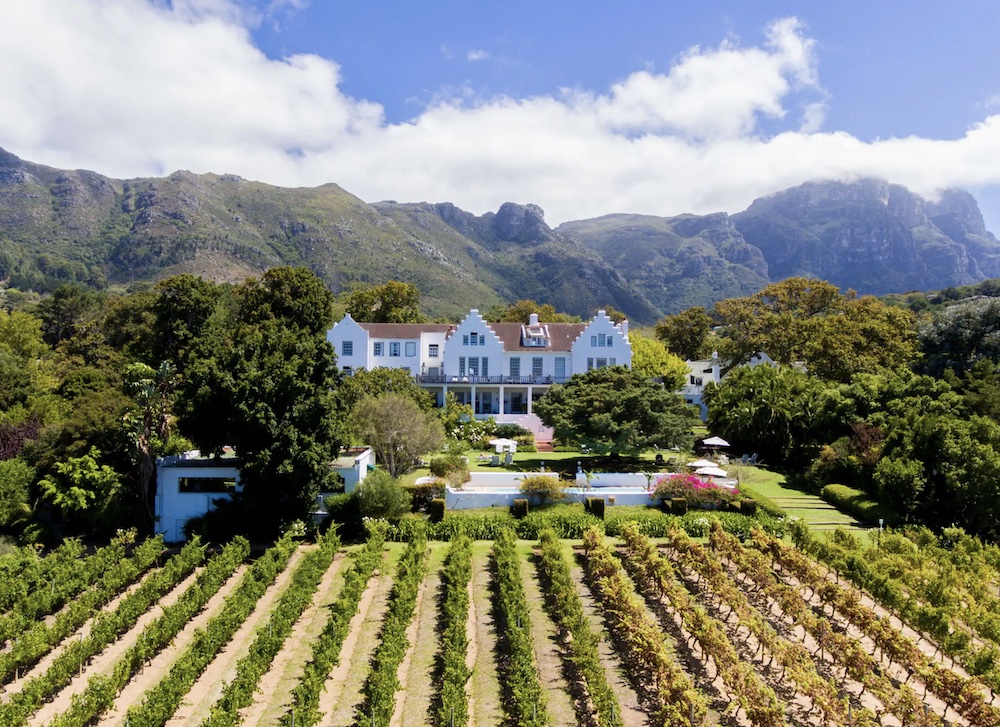 a large white house with a large garden and mountains in the background