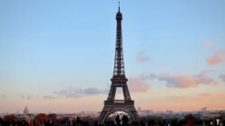 a large metal tower with people walking around with Eiffel Tower in the background