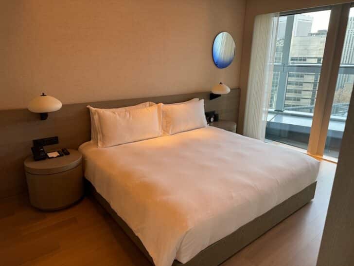 a bed with white sheets and a round mirror next to a window