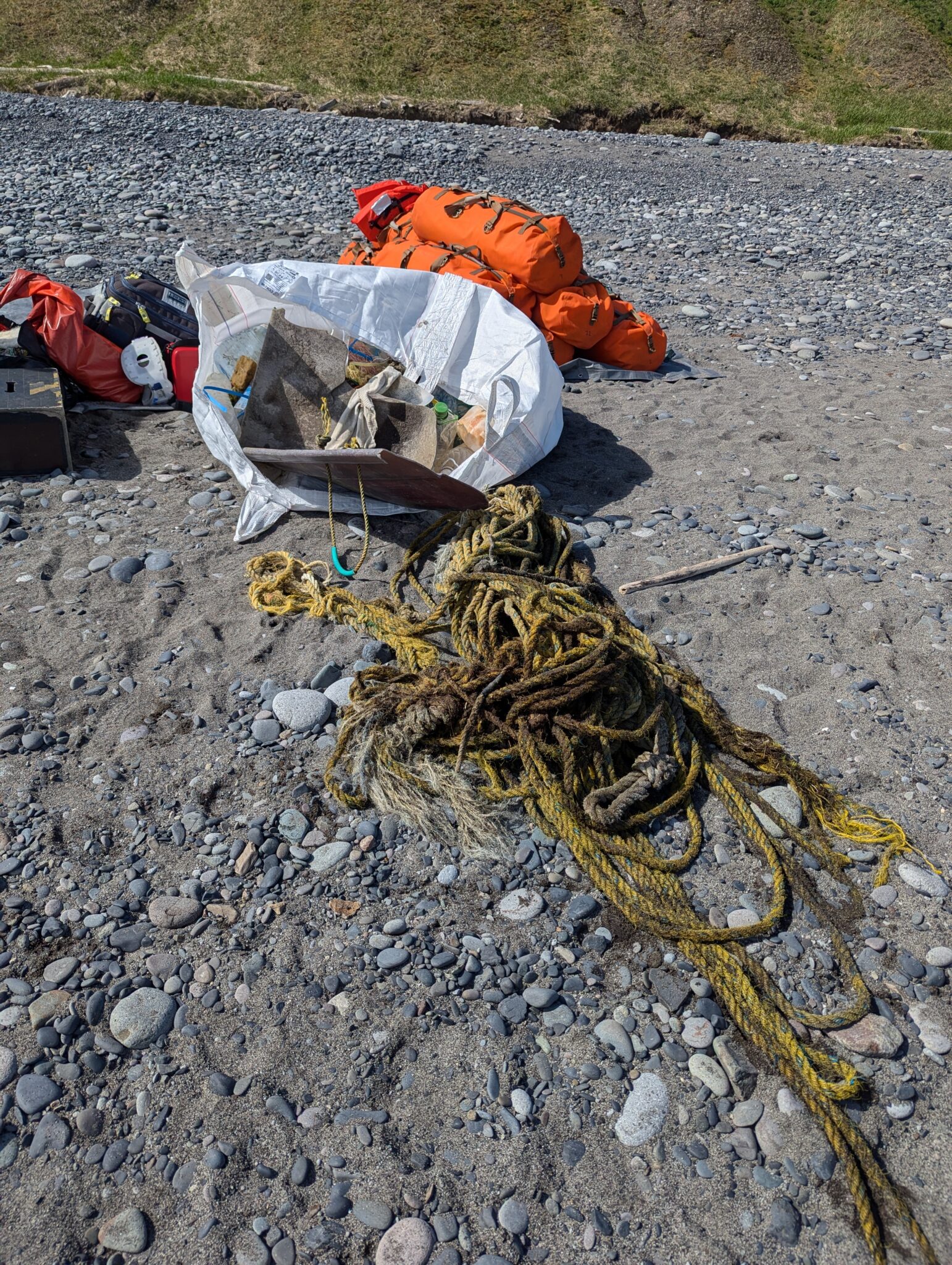 a pile of ropes and orange bags on a rocky beach