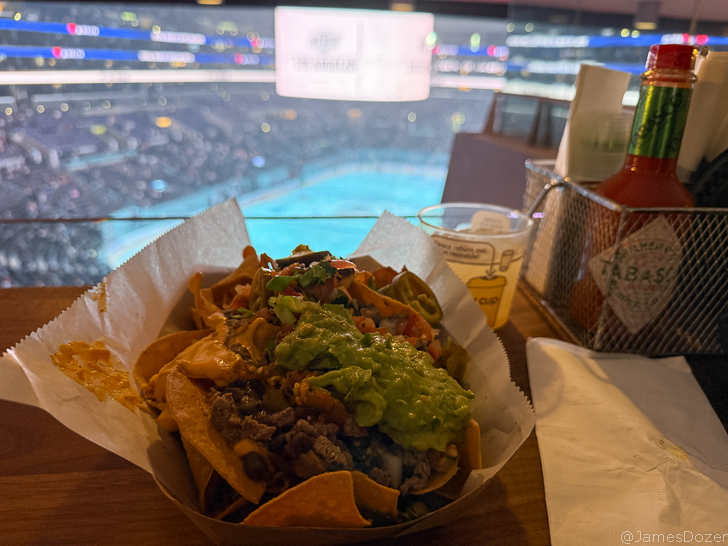 a bowl of nachos with sauces and a stadium in the background