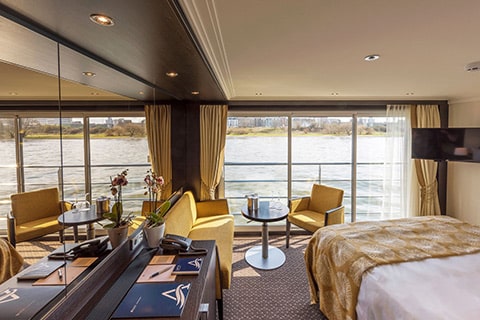 a room with a bed and a table and chairs by the water