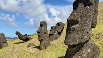 a group of stone statues on a hill with Easter Island in the background